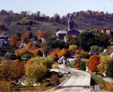 Autumn view of a town with colorful trees, a road, buildings, and a domed building atop a hill.