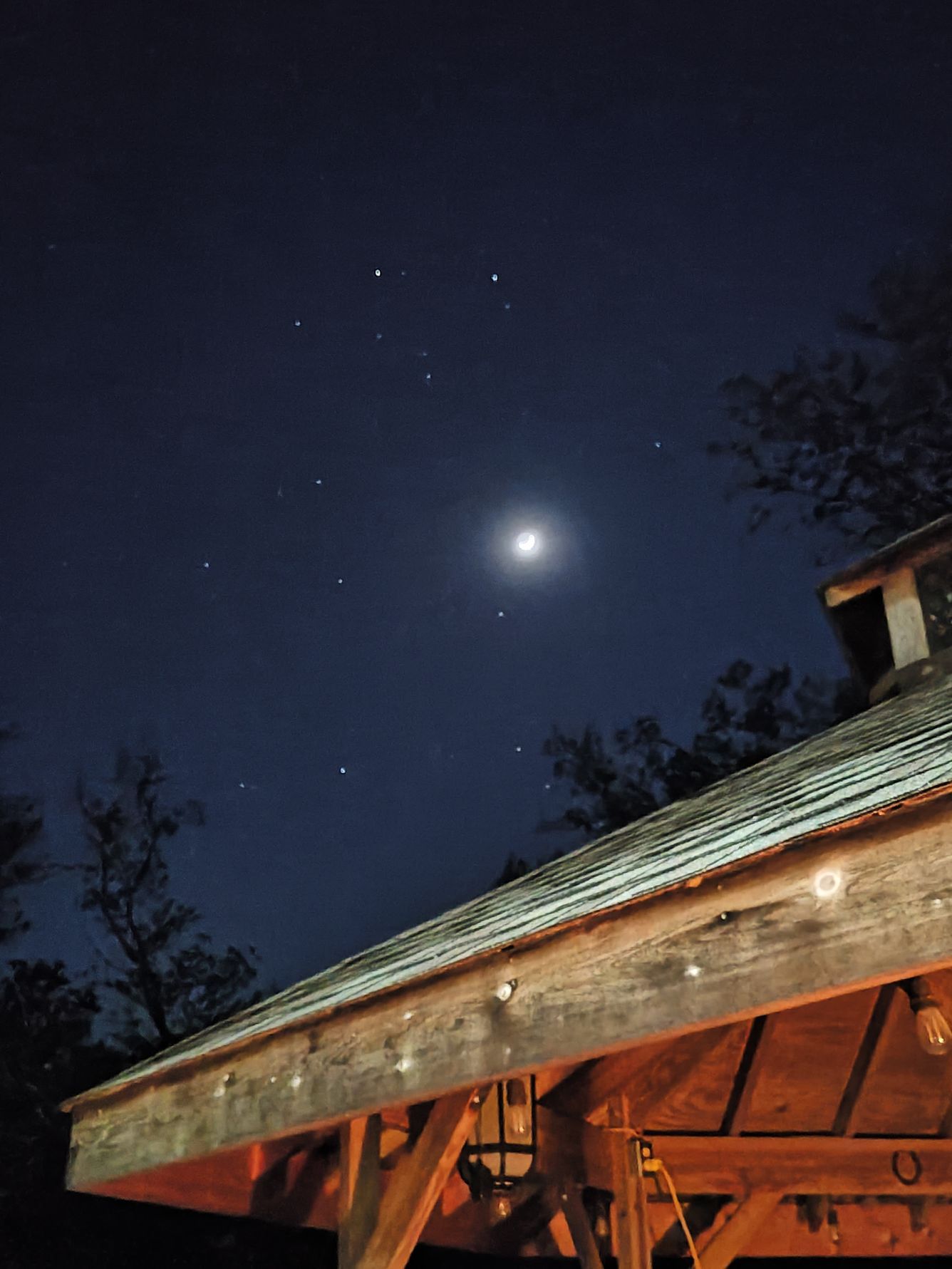 Night sky with the moon and visible stars above a wooden structure.