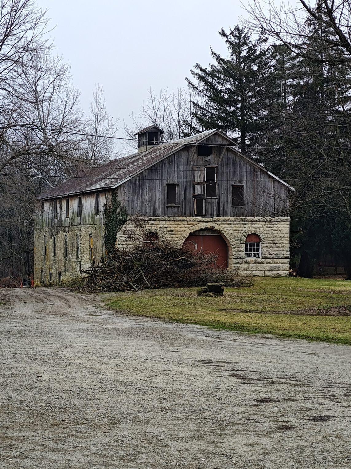 Old stone and wood barn with a weathered facade, red door, and overcast sky.