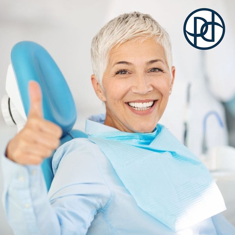 Woman in a dental chair gives a thumbs-up, smiling with a bib.