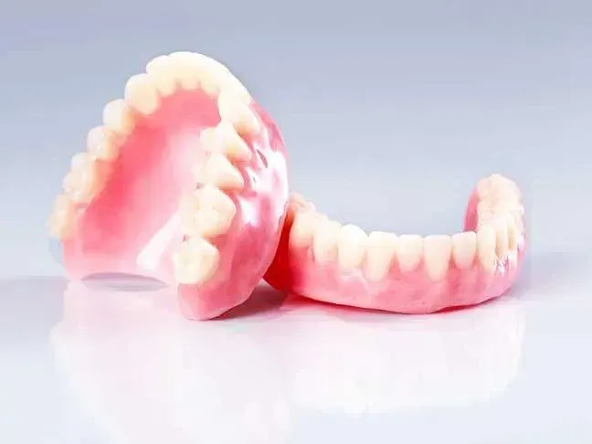 Set of dentures with pink gum and white teeth on a light background.