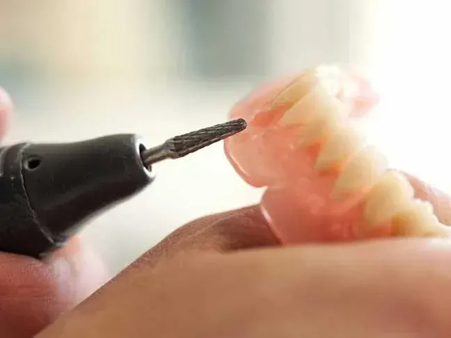 Close-up of a hand holding a dental drill near a set of false teeth.