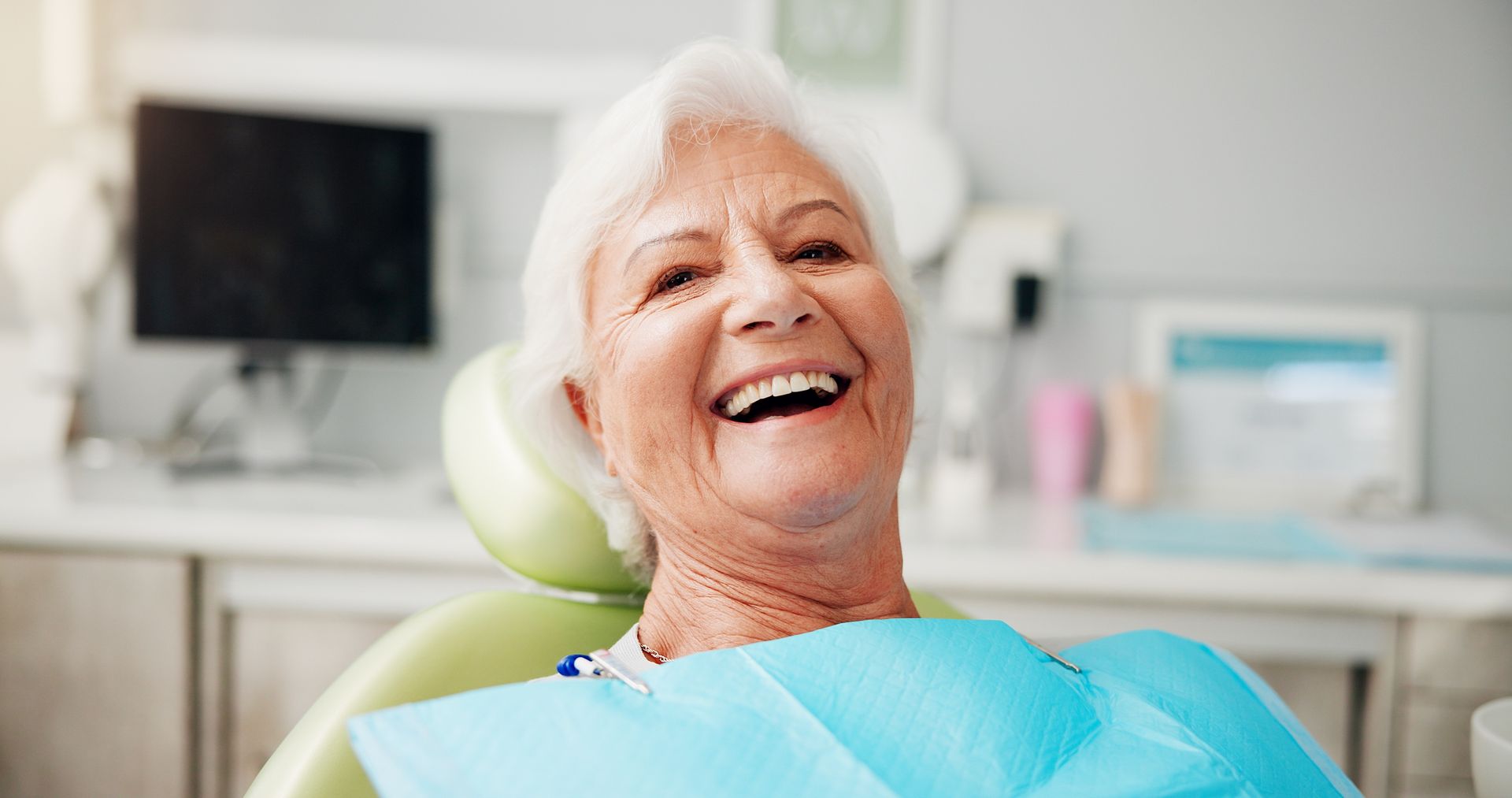 Close-up of a person smiling, showing new dentures. The person has a mustache and is wearing a bib.