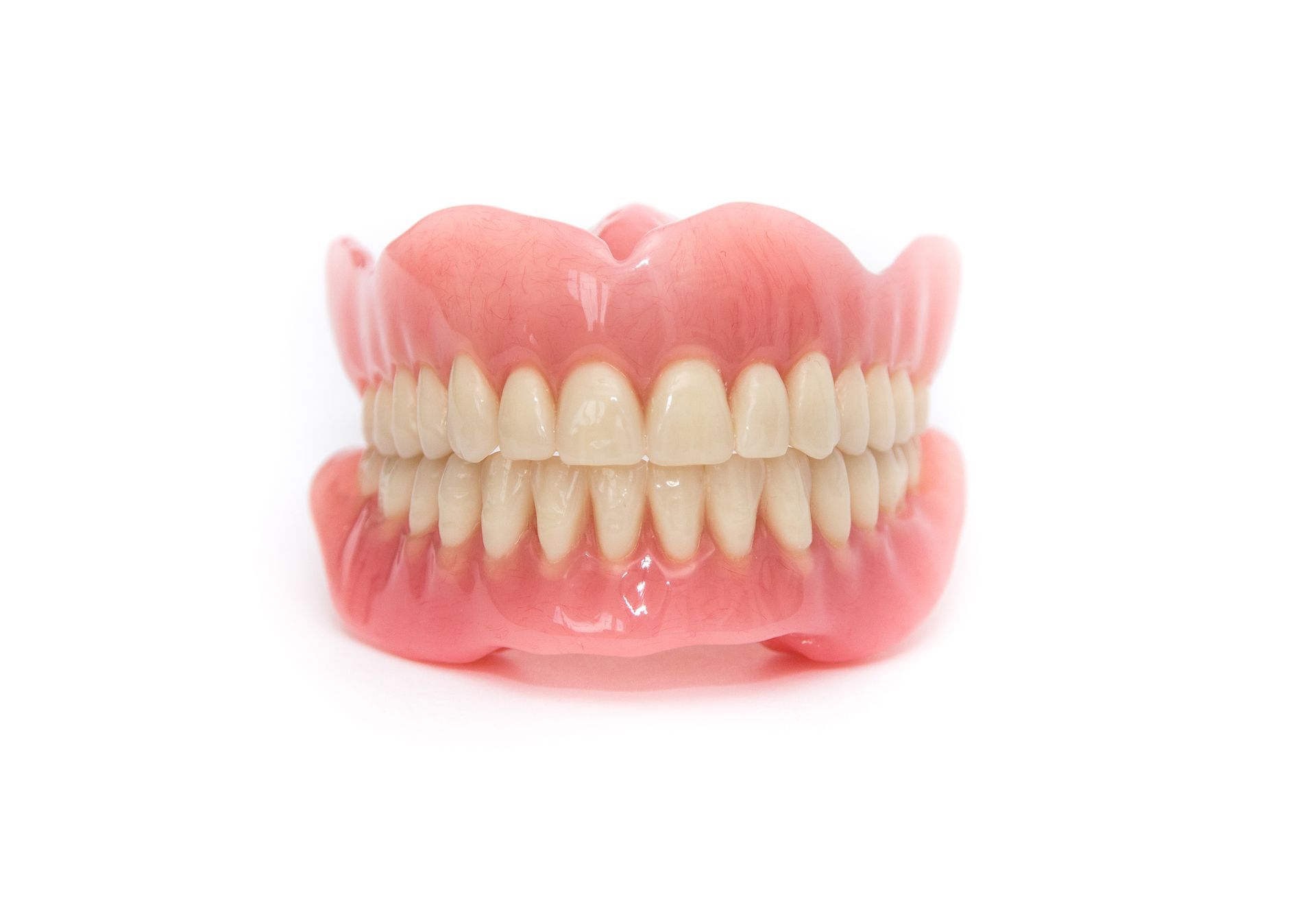 Hands in blue gloves holding a set of dentures, with pink gum-like material and white teeth.