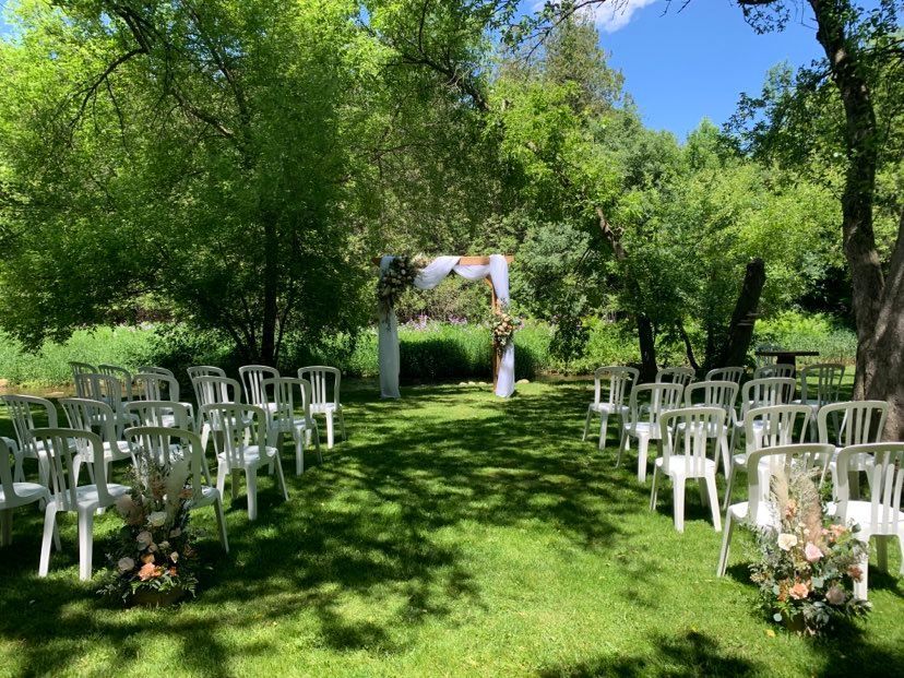 Wedding ceremony setup in a green grassy area with white chairs facing a decorated arch.