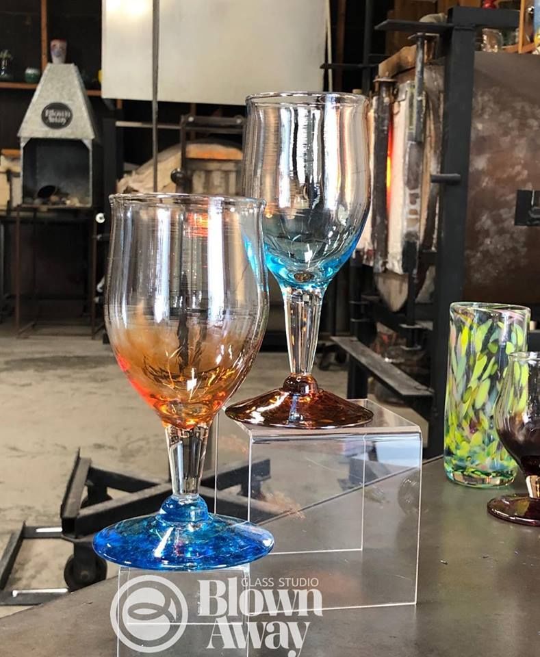 Two colored glass goblets on a clear stand in a glassblowing workshop.