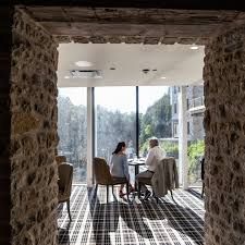 Two people seated at a table by a large window with a view, framed by a stone doorway.