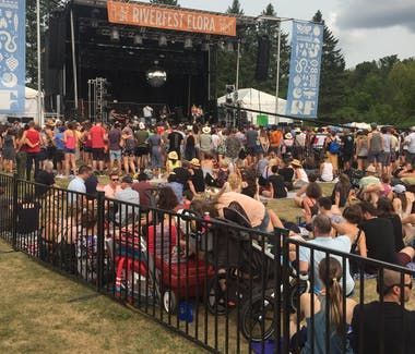 Crowd at outdoor music festival, stage in the background with 