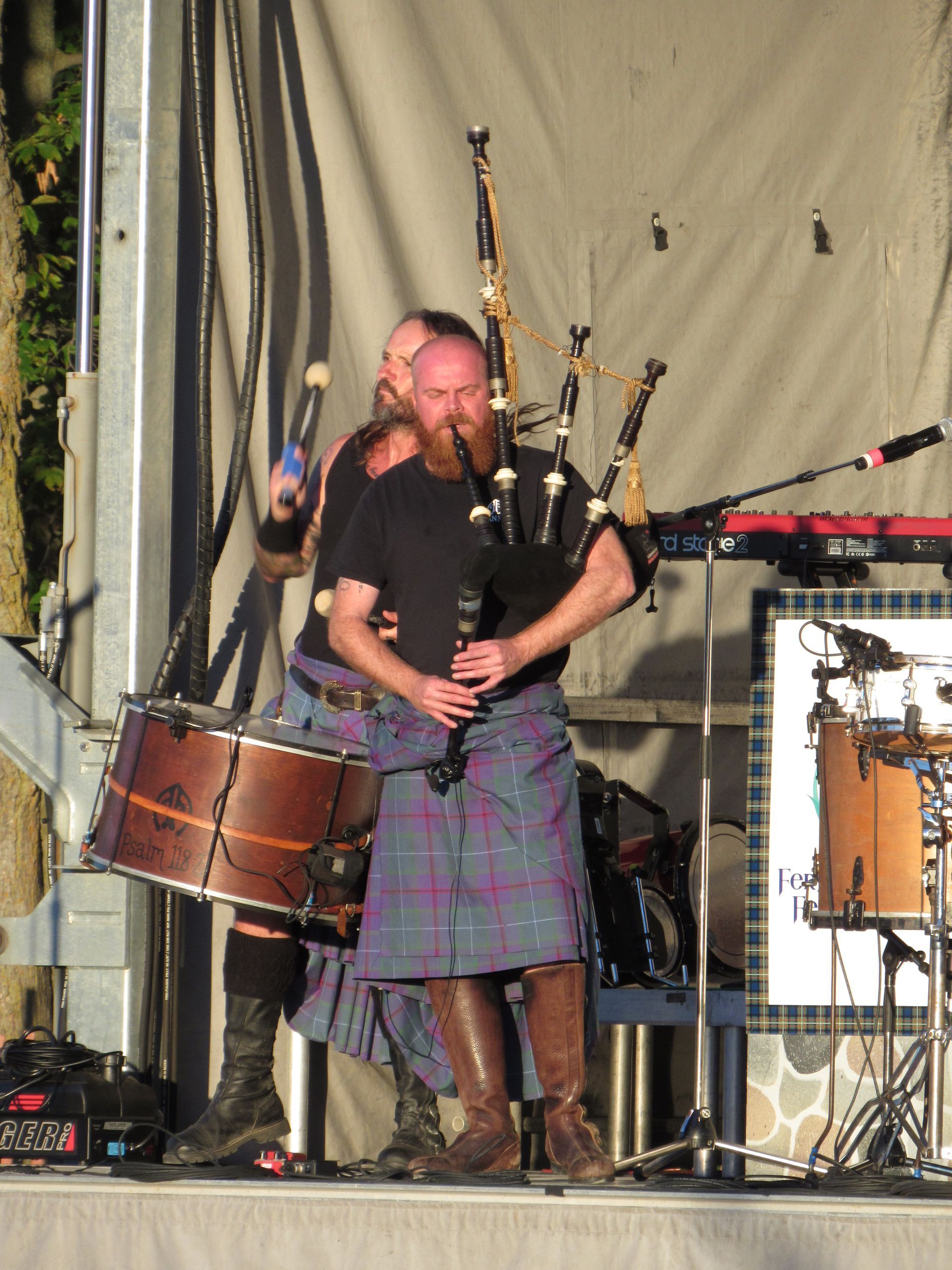 Two men in kilts perform on stage: one plays bagpipes, the other drums.