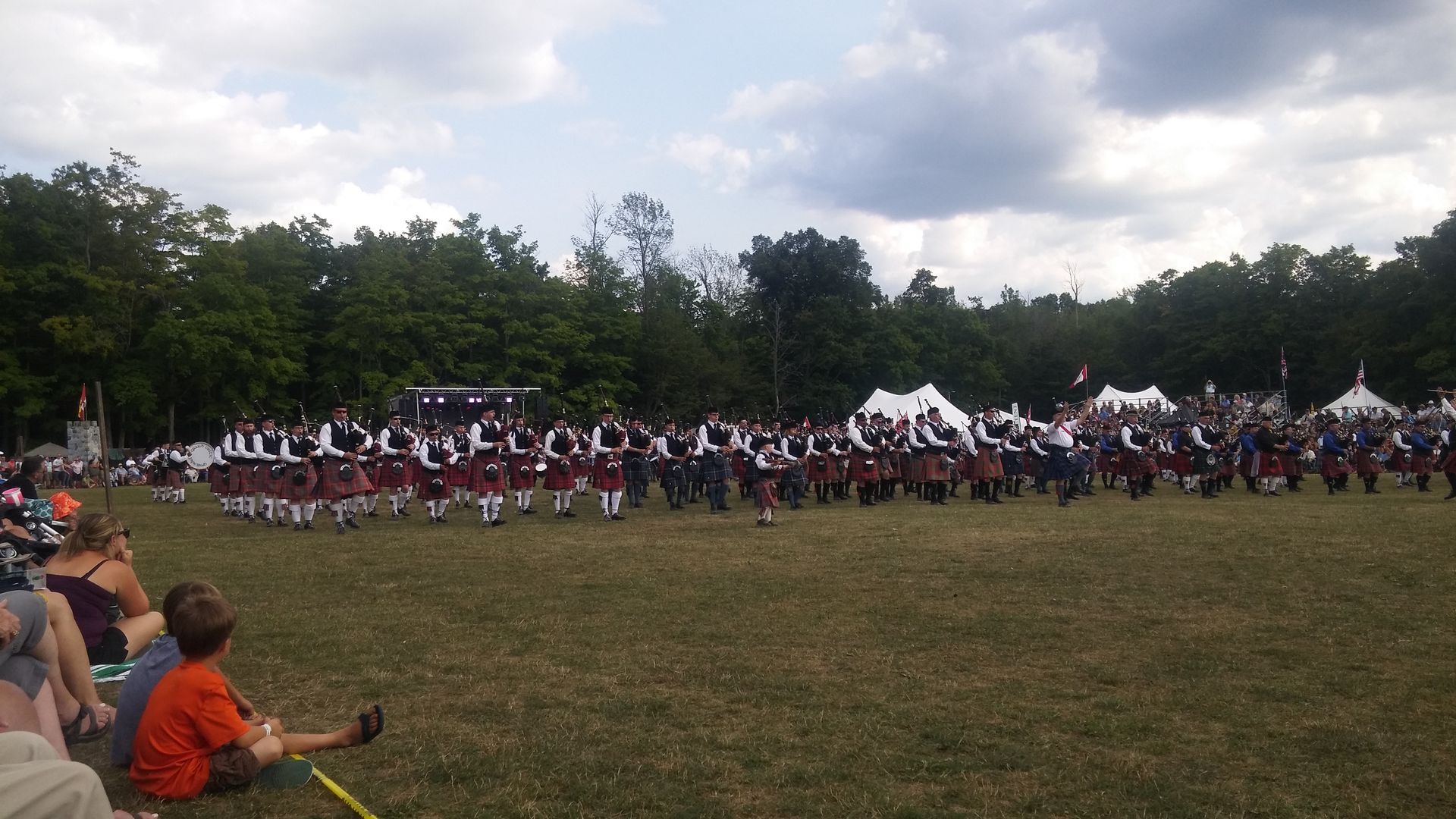 Scottish Highland dancers in kilts perform on a grassy field at an outdoor event.