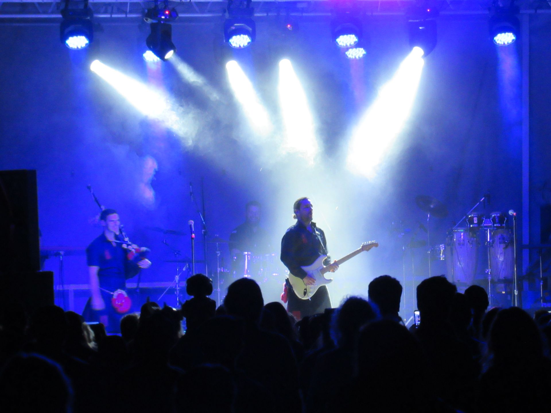 Band performing on stage with bright blue stage lights, crowd in foreground.