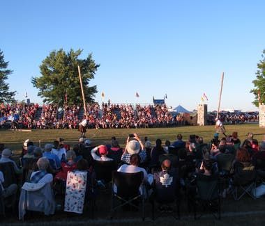 People watch a log-rolling competition at an outdoor event; competitors stand on logs.