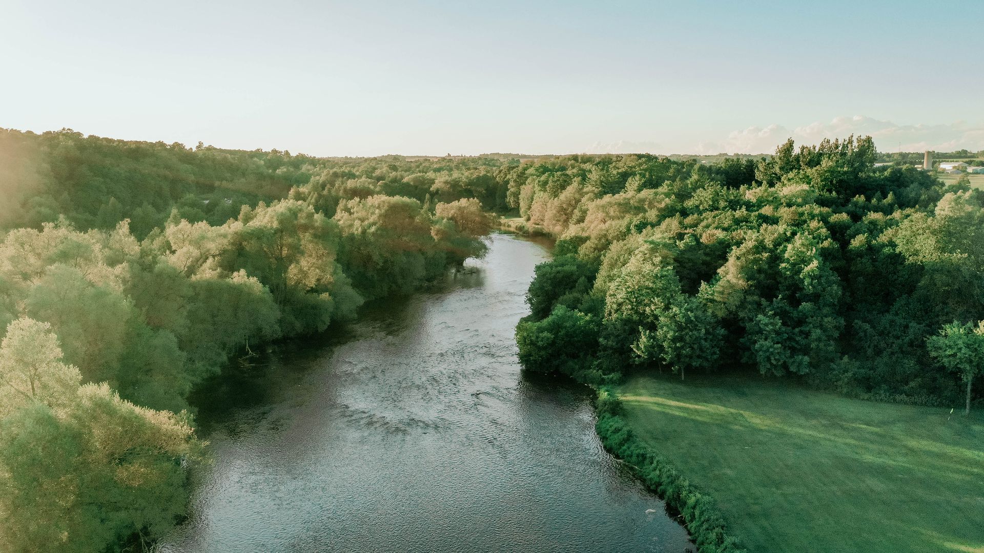 River flows through lush green trees, bathed in warm sunlight.
