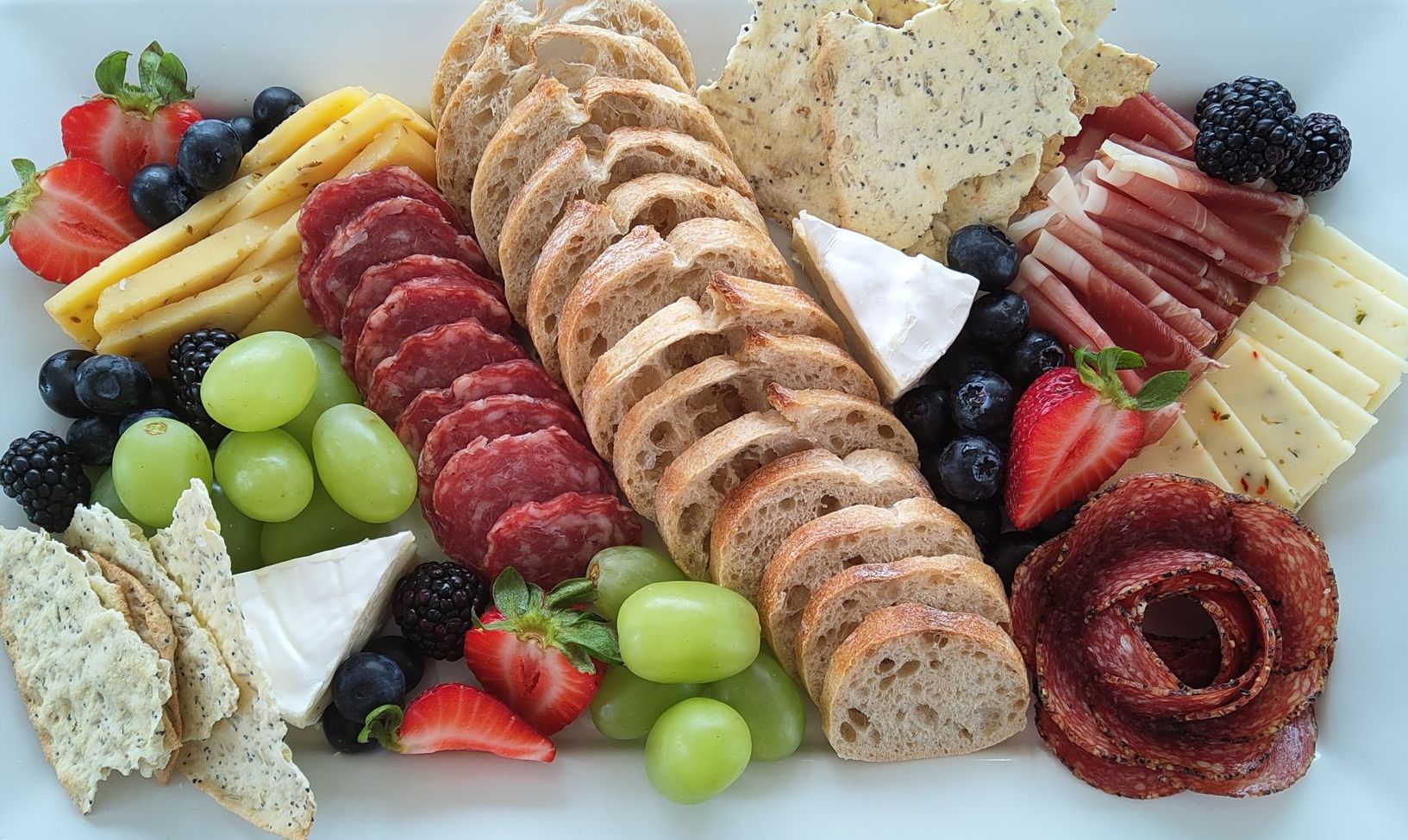 Charcuterie board with sliced meats, cheeses, bread, crackers, grapes, berries.