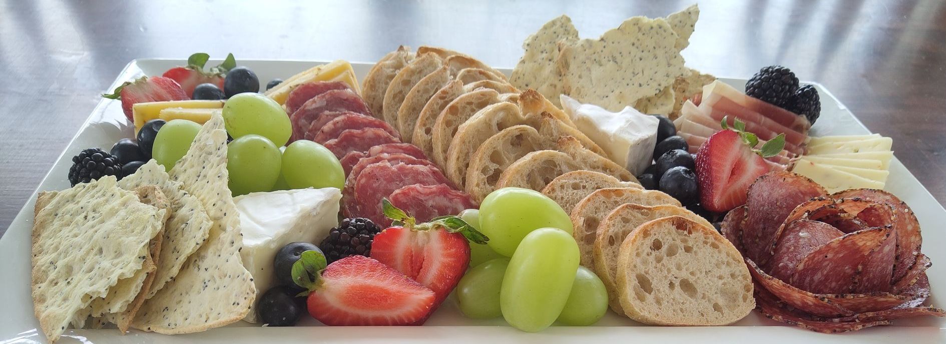Charcuterie board: crackers, fruit, cheese, and cured meats arranged on a white platter.