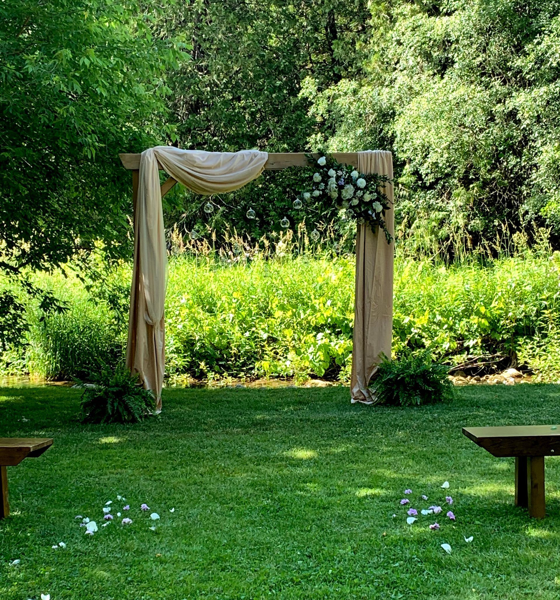Wedding ceremony arch with draped fabric and flowers in a green grassy outdoor setting.