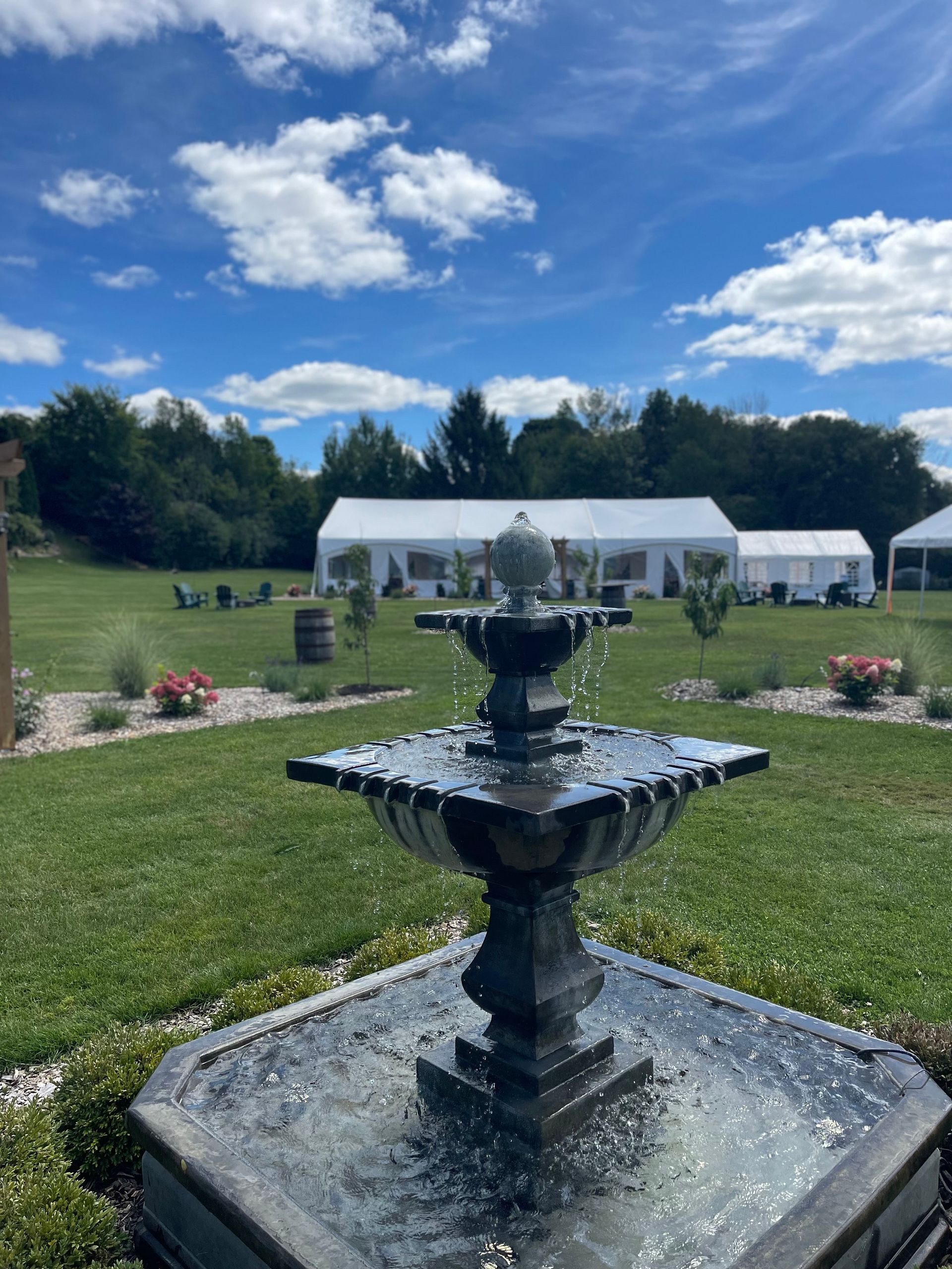 Stone fountain in a grassy field with a white event tent and blue sky in the background