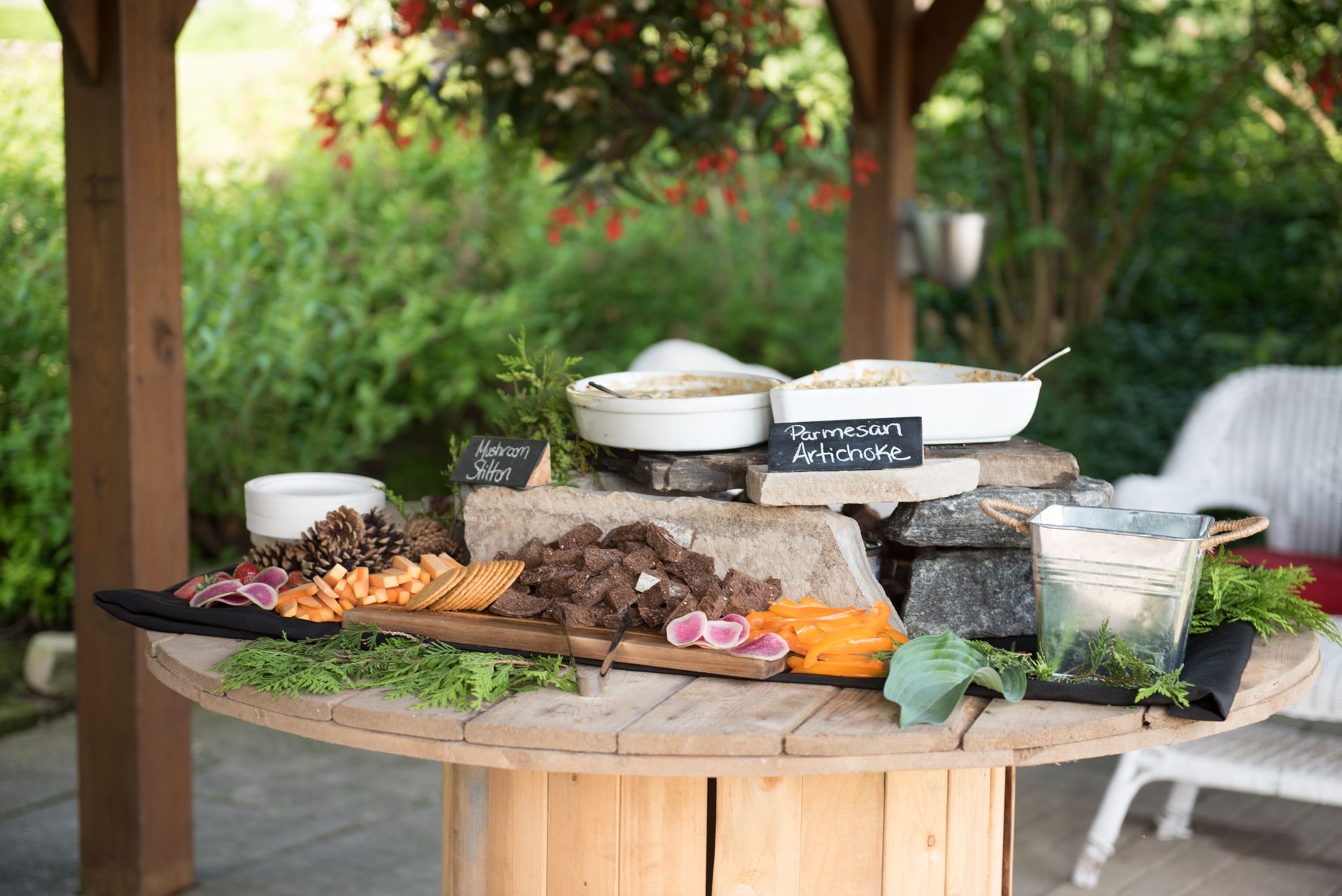 Outdoor food display on a wood table with appetizers and dips under a gazebo.
