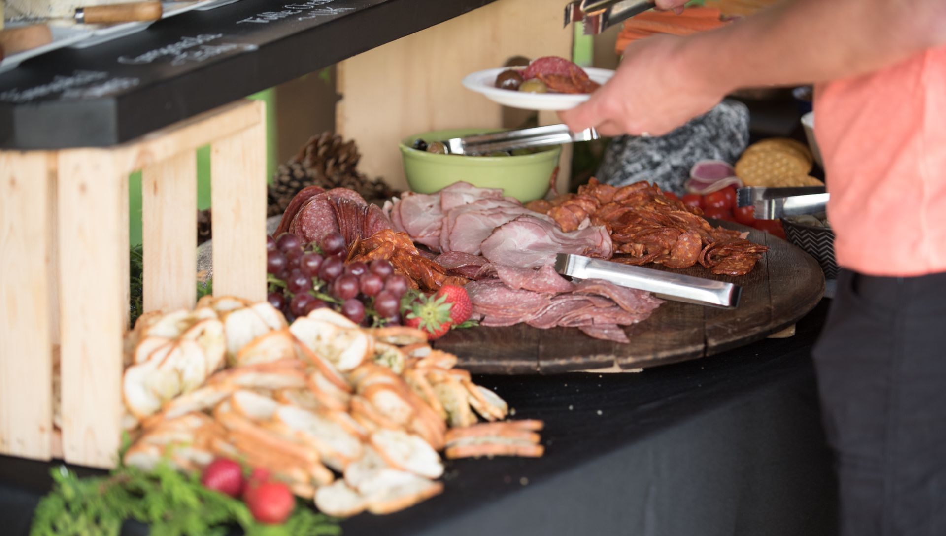 Buffet spread with meat, bread, and fruit. Person taking food with tongs.