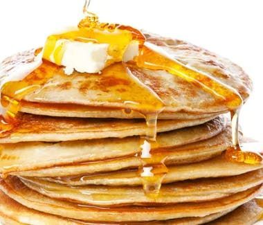 Stack of pancakes with melting butter and syrup being poured over them.