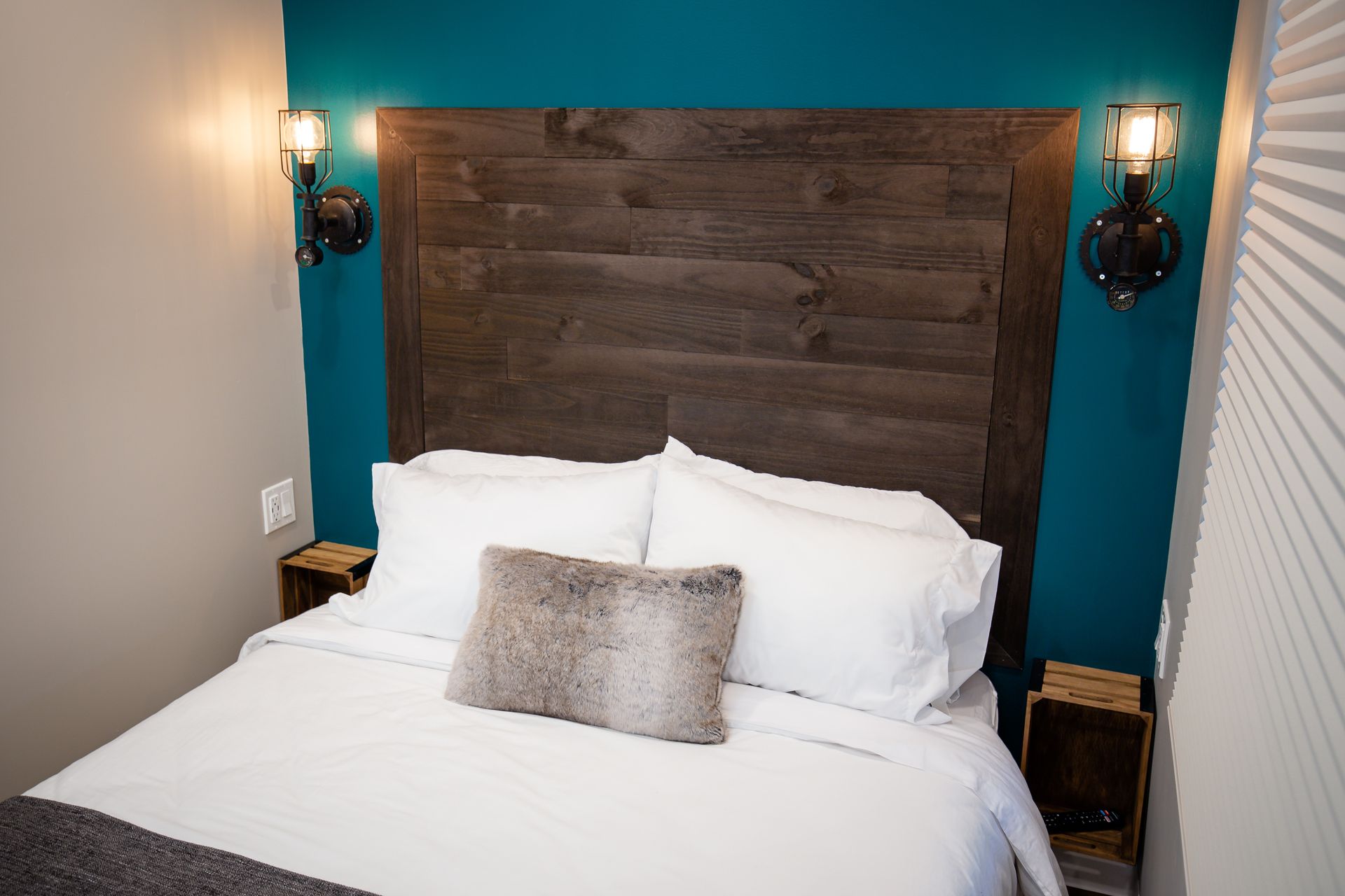 Small bedroom with a bed, wooden headboard, teal accent wall, and sconce lighting.