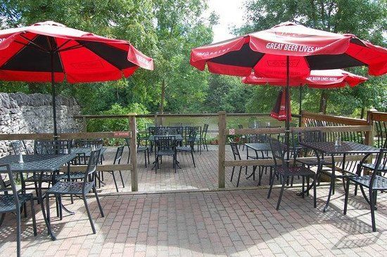 Outdoor patio with red umbrellas, tables, and chairs, overlooking a body of water.
