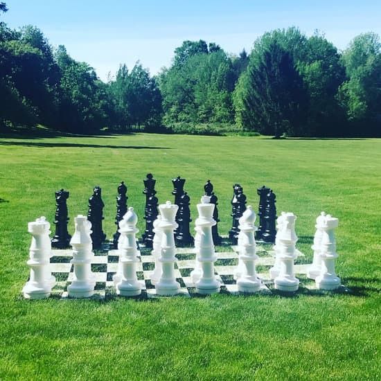 Large black and white chess pieces set up on a grass lawn with trees in the background.
