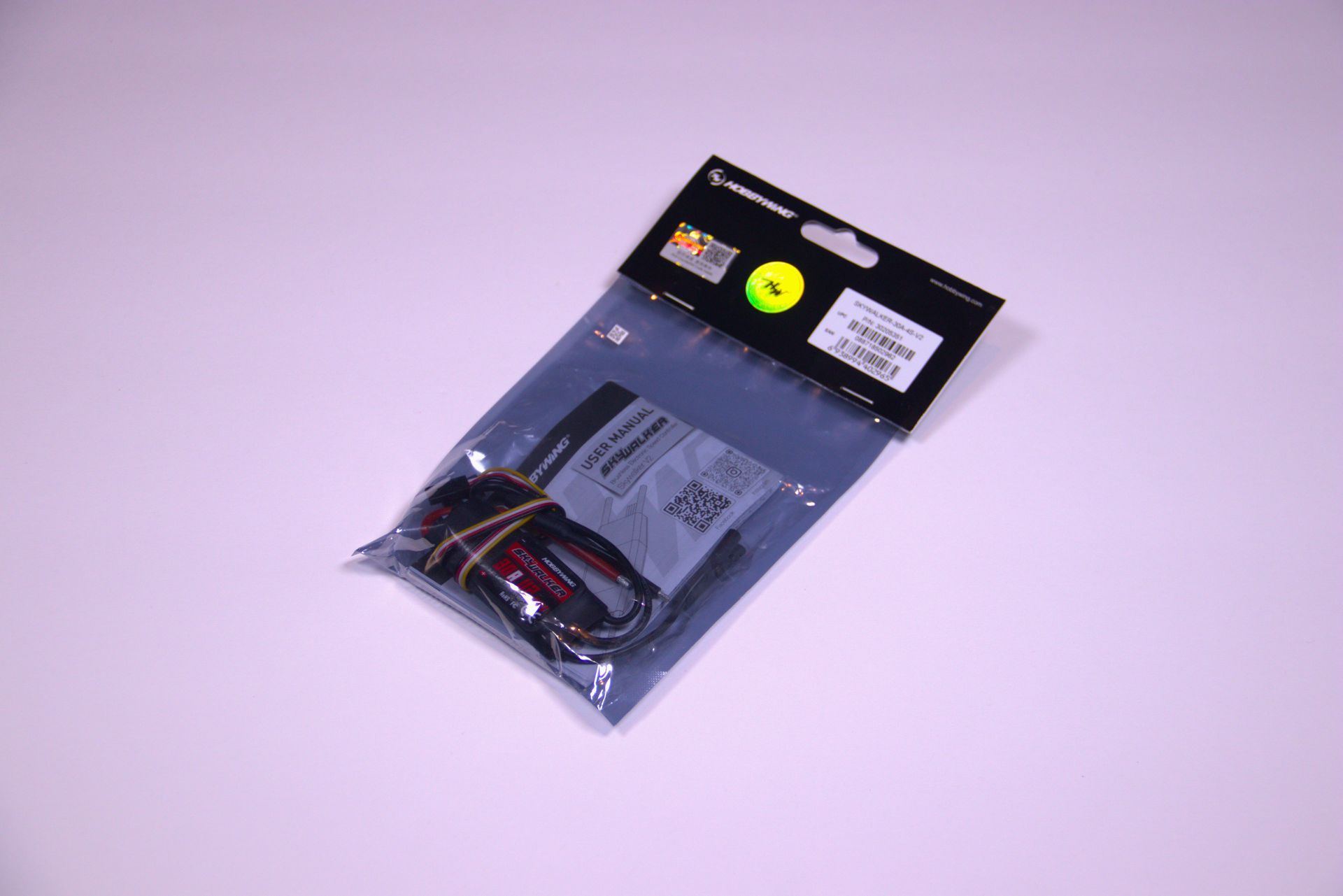 Clear plastic electronics accessory package with black label, shown on a light purple background