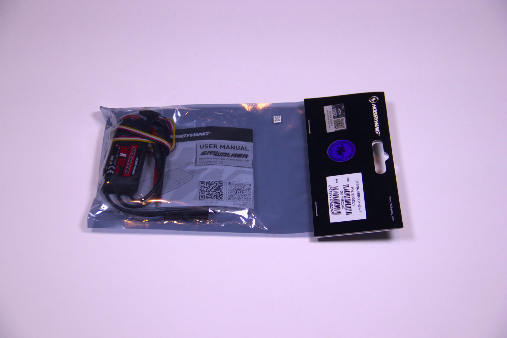 Clear plastic electronics accessory package with black label, shown on a light purple background