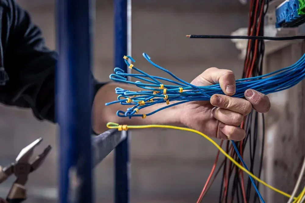Hands organizing blue and yellow electrical cables in a wiring panel