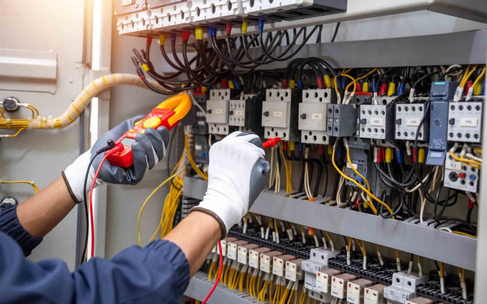 Technician inspecting electrical control panel wiring with tools and gloves