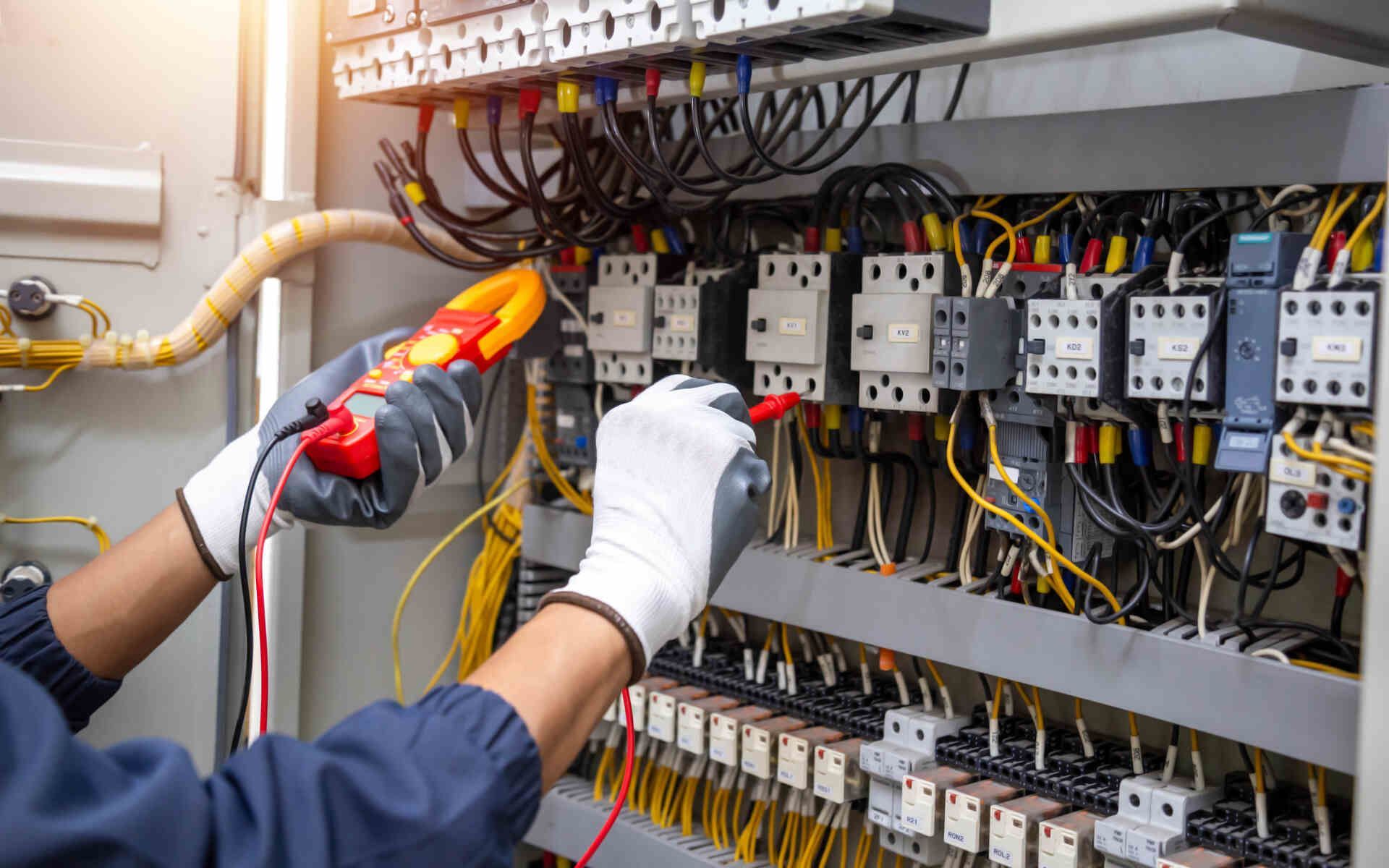 Technician wiring electrical control panel with gloves and insulated tools.