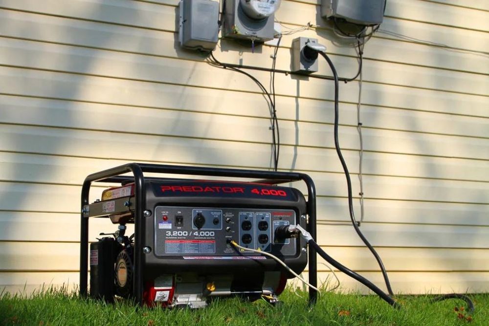 Portable generator outside a house beside utility meters, with cables running to the wall.