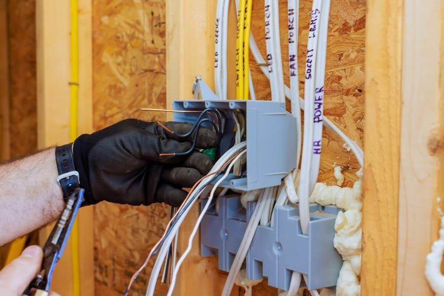 Gloved hand wiring an electrical box in a wall with exposed insulation and cables