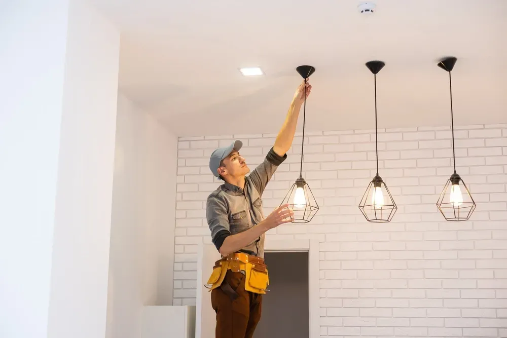 Electrician adjusting a ceiling light in a white room with three pendant fixtures