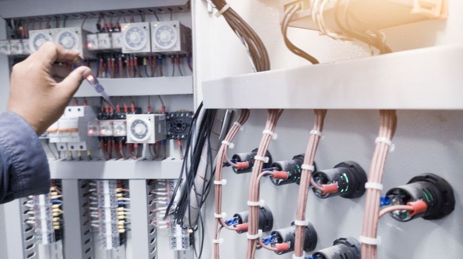 Electrical panel with exposed wiring; a hand adjusting components on the left side.