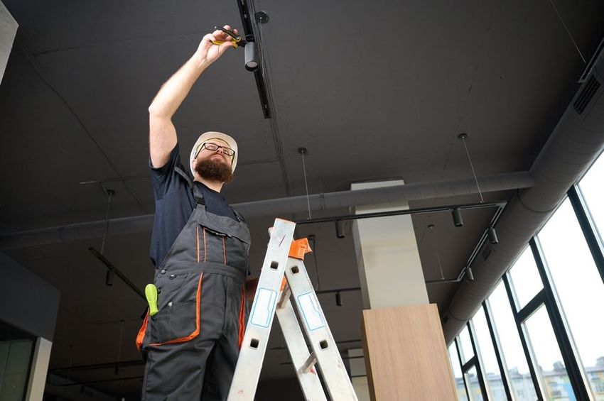 Worker on a ladder installing a ceiling fixture in a modern interior