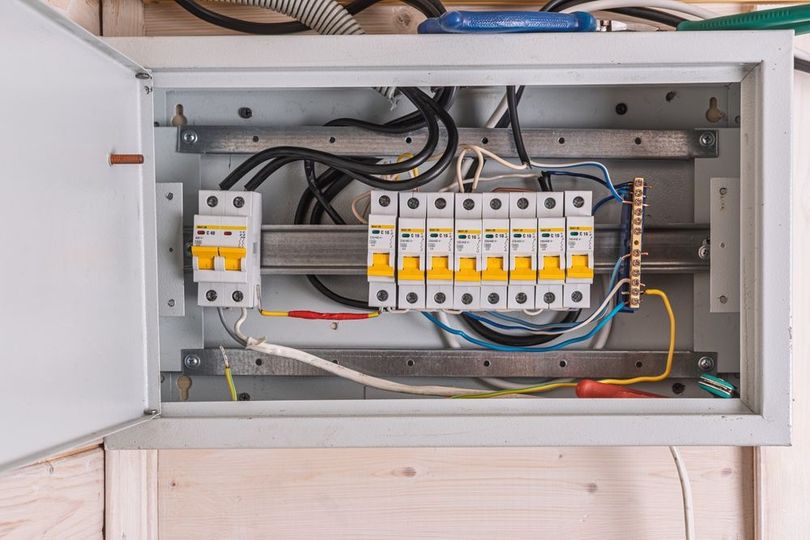 Open electrical panel with circuit breakers and wiring inside a gray metal box.