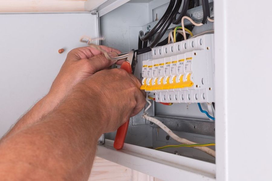 Hands wiring an electrical circuit breaker panel with red tools.