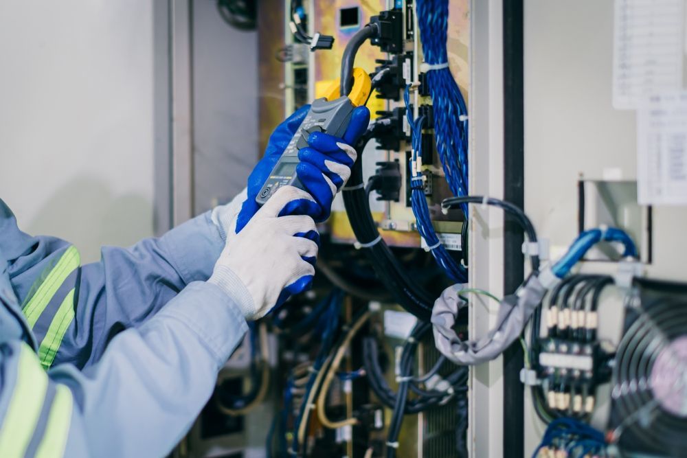 Technician in gloves using tools to inspect blue industrial machinery in a factory.