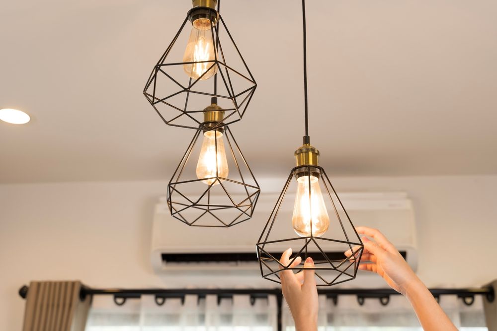 Three geometric pendant lights hanging from a ceiling, with hands adjusting one lamp