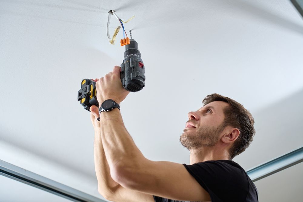 Man using a drill to install a ceiling fixture indoors