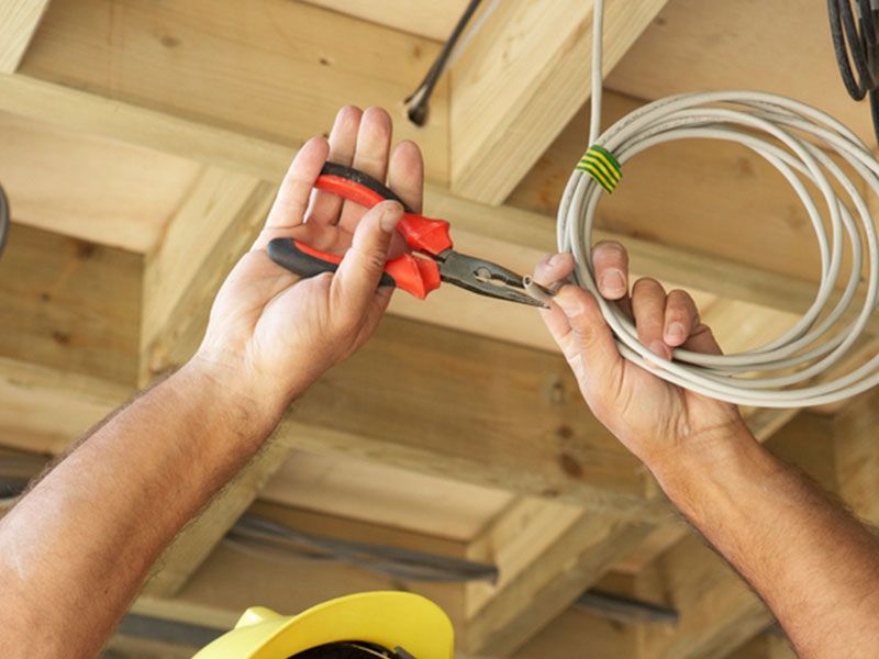 Hands using red-handled wire cutters to cut a coiled cable under wooden beams