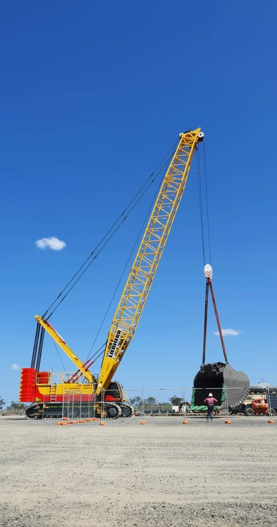 A Large Yellow Crane Is Lifting A Large Object In A Dirt Field — SureLift Crane Hire In Bowen, QLD