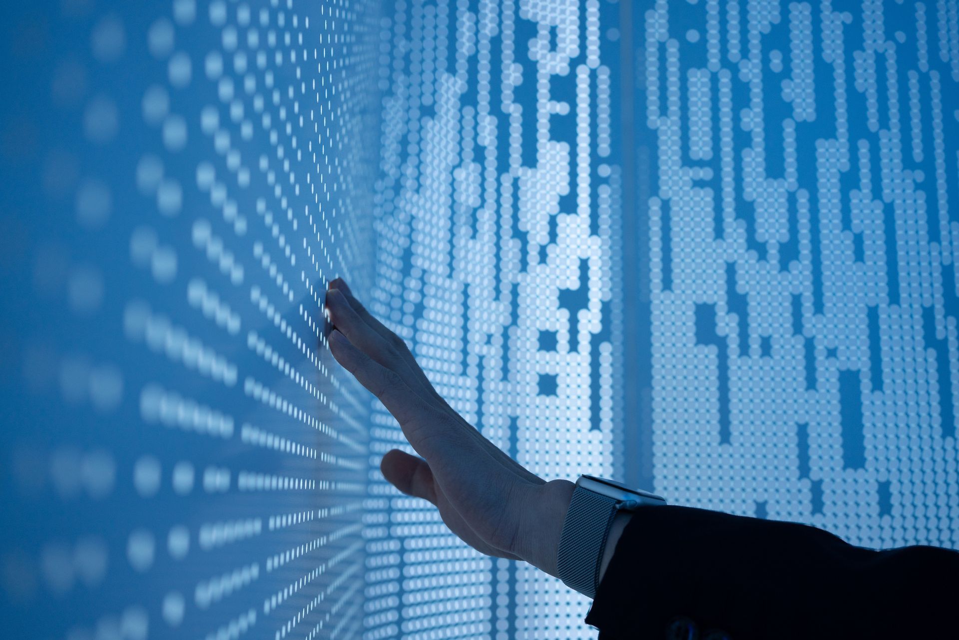 Hand touching a blue wall with a pattern of dots and vertical lines.
