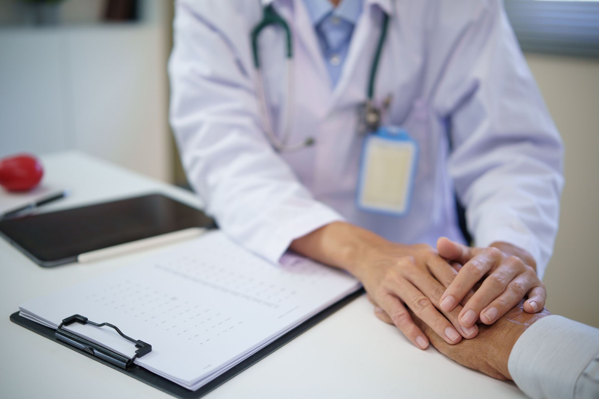 Doctor's hands on a patient's hand; a supportive gesture. White lab coat, stethoscope, clipboard, tablet. Doctor's hands on a patient's hand; a supportive gesture. White lab coat, stethoscope, clipboard, tablet.