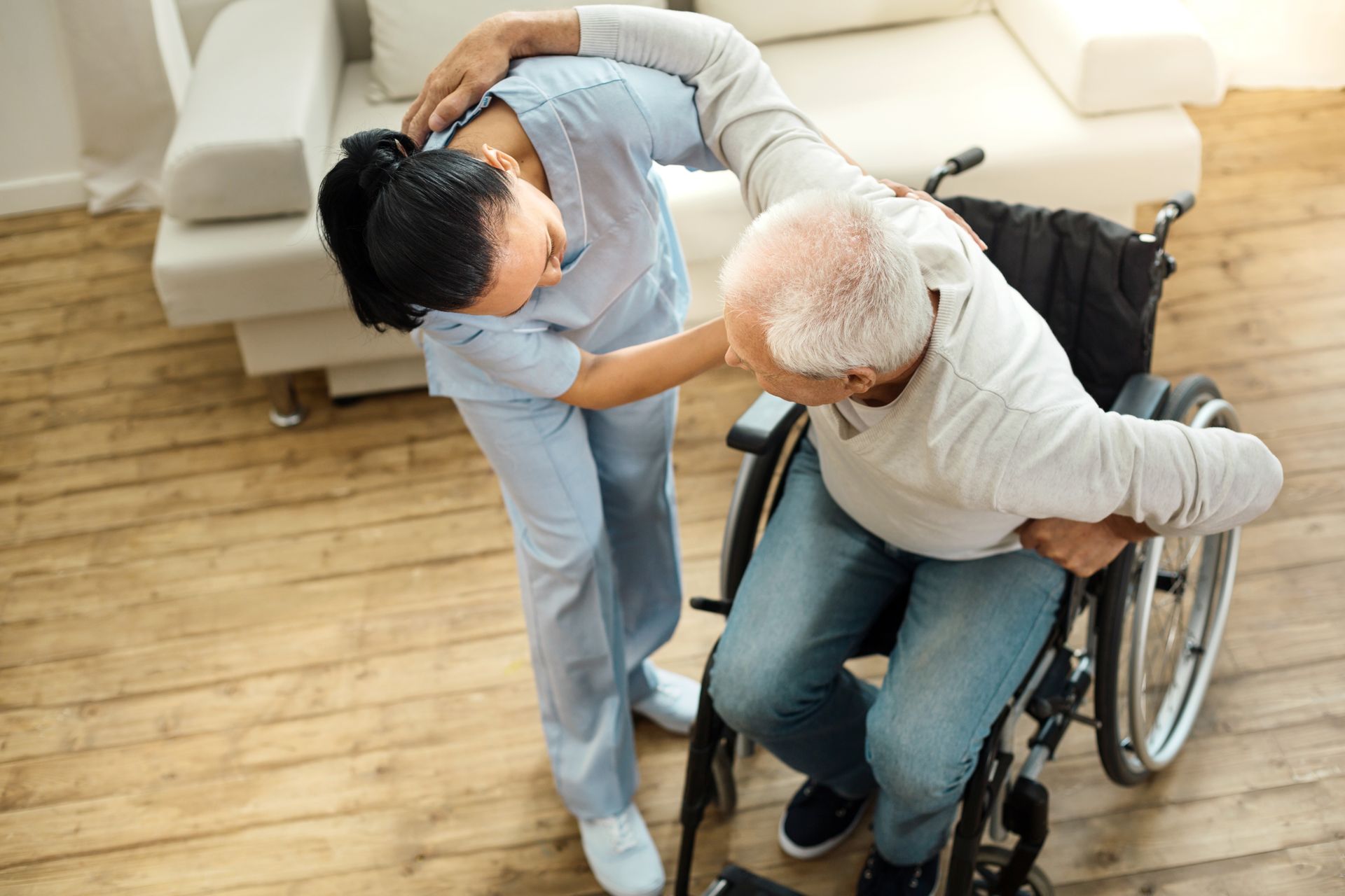 Caregiver assisting a person in a wheelchair; indoor setting, helping to stand up