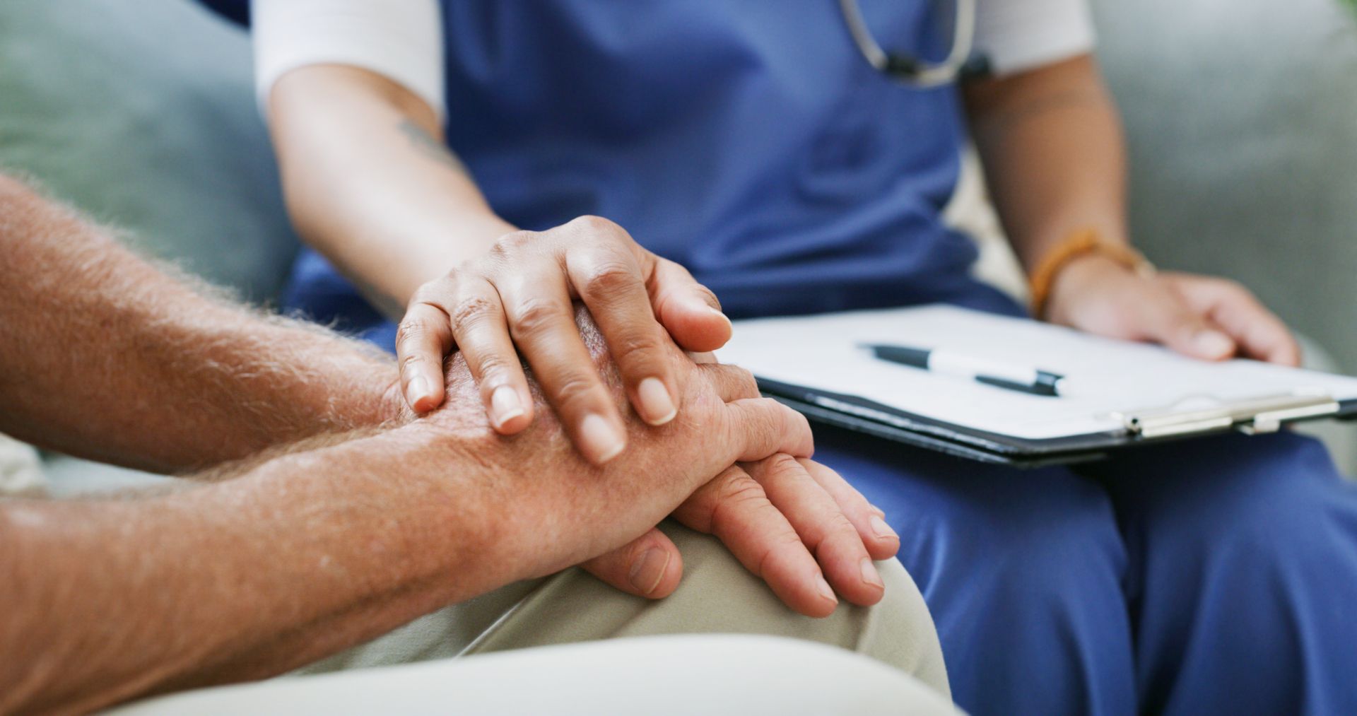 Nurse's hand comforting patient's hands while holding a clipboard Nurse's hand comforting patient's hands while holding a clipboard