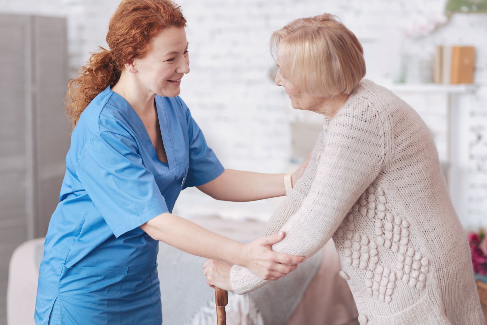 Caregiver in blue scrubs assists an elderly person using a cane; indoors Caregiver in blue scrubs assists an elderly person using a cane; indoors