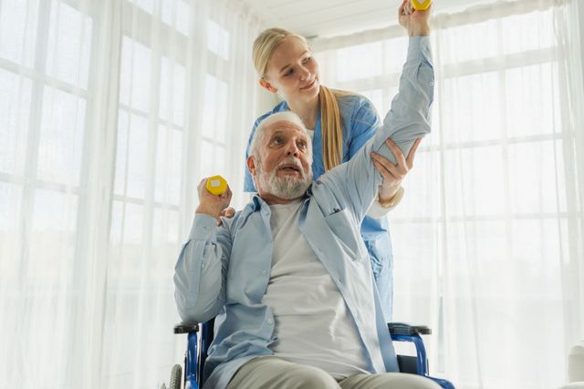 Woman assists seated man with weights, indoors by window